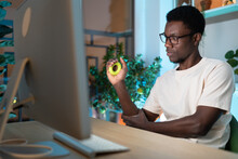 Young African Man Freelancer Exercising With Silicone Grip Ring At Cozy Home Office, Remote Worker Doing Hand Exercises While Resting From Computer At Workplace. Carpal Tunnel Syndrome Prevention