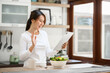 © interstid - Smiling beautiful asian woman using digital tablet in the kitchen at home