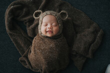 Happy Newborn Baby Wrapped In Cocoon Sleeping With Cute Knit Bear Hat