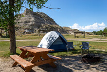 Simple Tent Campsite With Picnic Table In Dinosaur Provincial Park Southern Alberta, Grass And Large Rock Formation In Background With Blue Sky
