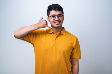Wall Mural - Young asian man smiling doing phone gesture with hand and fingers like talking on the telephone. Communicating concepts.