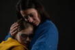 © Halfpoint - Sad mother hugging her daughter, both wearing Ukrainian national colors on black background.