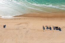 Aerial View Of A Group Of Four Wheel Drives Parked In A Sandy Beach With Waves Gently Washing Ashore