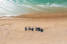 Aerial View Of A Group Of Four Wheel Drives Parked In A Sandy Beach With Waves Gently Washing Ashore