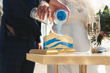 The newlyweds together pour white and blue sand into a vase