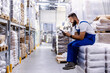 © dusanpetkovic1 - The storage worker is sitting on the pile of bags with flour and he is using the tablet for checking on orders.