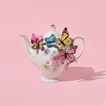 Spring Creative Layout With English Garden Teapot With Colorful Butterflies On Pastel Pink Background. 80s, 90s Retro Romantic Aesthetic Summer Concept. Minimal Surreal Fashion Tea Idea.