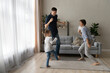 © fizkes - Happy active two generations family dancing to music in modern renovated living room. Joyful millennial couple father mother having fun with cheerful small adorable child daughter on weekend at home.