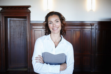 Wall Mural - Ready for the judge. Attractive female legal person standing with her arms folded and smiling widely in the courtroom.