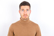 © Roquillo - Displeased upset young caucasian man wearing grey turtleneck over white background frowns face as going to cry, being discontent and unhappy as can't achieve goals,  Disappointed model has troubles