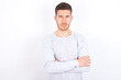 © Roquillo - Self confident serious calm young caucasian man wearing grey sweater over white background stands with arms folded. Shows professional vibe stands in assertive pose.