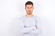 © Roquillo - Gloomy dissatisfied young caucasian man wearing grey sweater over white background looks with miserable expression at camera from under forehead, makes unhappy grimace