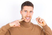 Young Caucasian Man Wearing Grey Turtleneck Over White Background Holding An Invisible Aligner And Pointing To Her Perfect Straight Teeth. Dental Healthcare And Confidence Concept.