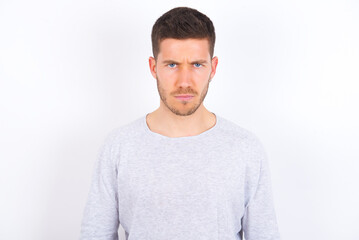 Offended dissatisfied young caucasian man wearing grey sweater over white background with moody displeased expression at camera being disappointed by something