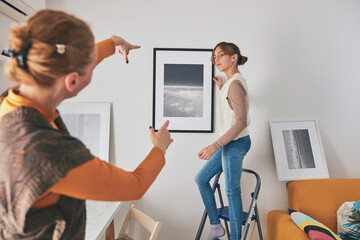 Mother and daughter hanging pictures and photos at home.