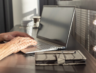 Poster - Man hands closeup typing on laptop keyboard. Bisinessman, freelancer or student sitting at cafe table with notebook and takeaway cup and working or studying. City lifestyle concept. High quality photo