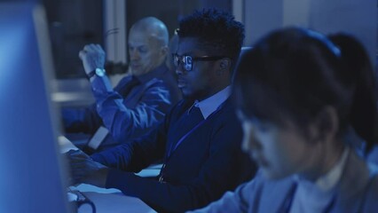 selective focus of young black man sitting on chair at desk in dark modern office, using computer at
