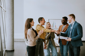 Memembers of creative team shaking hands while working in the modern office