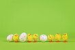 Small decorative easter chickens and eggs in a row on green background