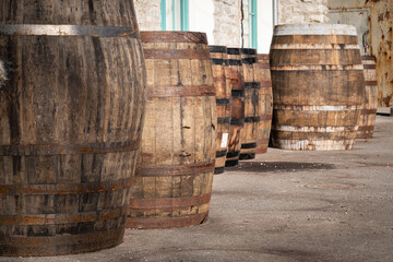 Old wooden barrels or casks at brewery backyard on a sunny day. Wine or beer oak vintage containers with stone wall texture background. Factory warehouse