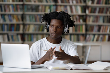 Concentrated young African American male student in headphones looking at computer screen, discussing educational material or lecture with teacher using video call application, e-learning concept.