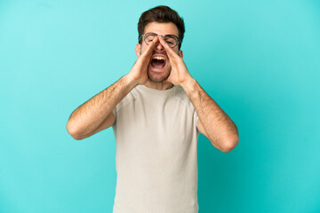 Wall Mural - Young caucasian handsome man isolated on blue background shouting and announcing something