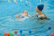© ninelutsk - Toddler child learning to swim in indoor swimming pool with teacher. Floating in the water, balancing and general physical activity for kids, early development. Boy kid trained to kick legs and float