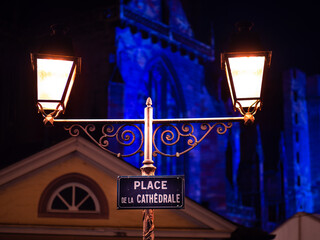 Place de la cathedrale - Cathedral Square at night in Colmar with a double street lamp. The cathedral in the background is blue illuminated - Christmas time