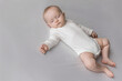 © fizkes - Serene peaceful sweet baby in white bodysuit sleeping on double bed, lying pn back on pale sheet. Few month sleepy infant child resting on soft mattress. Child care daily routine concept
