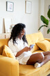 © CarlosBarquero - Vertical photo of a Woman sitting on the sofa at home using mobile phone