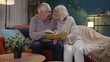 © Andrii Iemelianenko - Happy senior grandfather, grandmother relaxing talking enjoying leisure hobbies together at evening home, elderly husband grandpa reading book with old wife granny use magnifying glass sitting on sofa