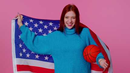 Redhead happy young woman 20s sportswoman basketball fan in blue sweater holding American USA flag doing winner gesture, dancing isolated on pink background. Workout sport motivation lifestyle concept