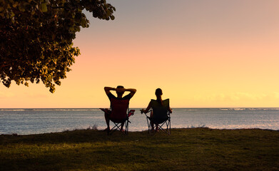 Couple relaxing together sitting on a beach chair enjoying the sunset nature view