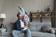 Happy cheerful dad holding excited funny preschool son kid in arms upside down, sitting on couch, laughing, having fun, playing active games with child, enjoying family leisure time, fatherhood