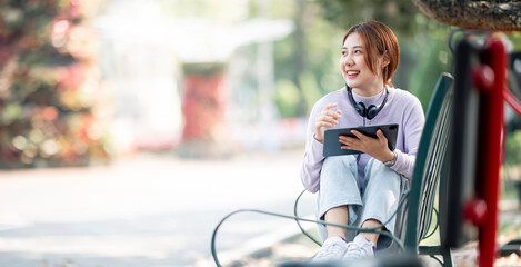 Happy young beautiful  student girl sitting outdoors in nature park using laptop computer.