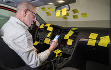 A Man Working In The Driver's Seat Of A Car Surrounded By Many To-do Notes.