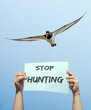 stop hunting. sign raised by female hands with white bird and blue sky