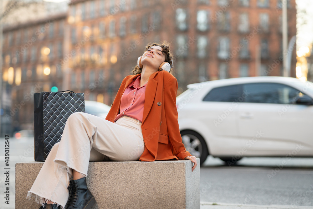 Young woman listening music through headphones sitting on bench