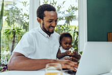 Smiling Father With Son Using Laptop In Dining Room