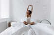© Westend61 - Woman sitting cross-legged with arms raised on bed at home