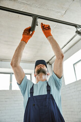 Wall Mural - Bearded young man fixing ceiling lamp in building