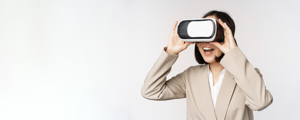 Amazed business woman in suit using virtual reality glasses, looking amazed in vr headset, standing over white background