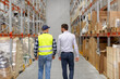 © Syda Productions - wholesale, logistic business and people concept - manual worker and businessman walking along warehouse