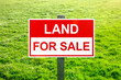 Land for sale sign in green grass field for housing development and construction