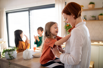 Wall Mural - Mother embracing her little daughter in kitchen at home.