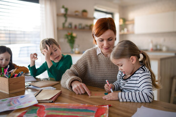 mother of three little children supervising them when diong homework at home.