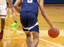 Rear View Of Basketball Player Dribbling The Ball Up Court During A Game