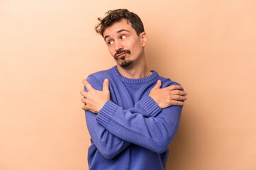 Wall Mural - Young caucasian man isolated on beige background hugs, smiling carefree and happy.