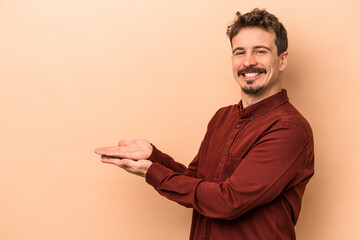Wall Mural - Young caucasian man isolated on beige background holding a copy space on a palm.