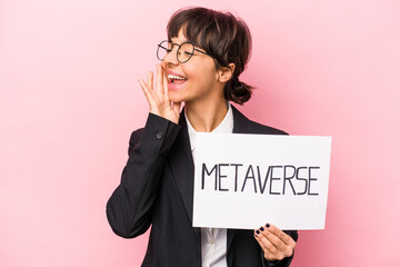 Wall Mural - Young hispanic business woman holding a metaverse placard isolated on pink background shouting and holding palm near opened mouth.